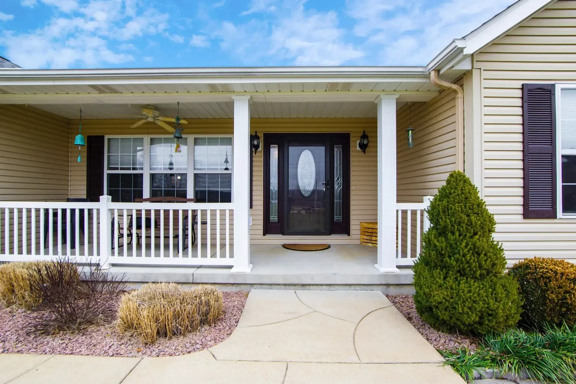 Front porch of a single-story home with white railings, dark entry door, and landscaped yard with evergreens and decorative gravel