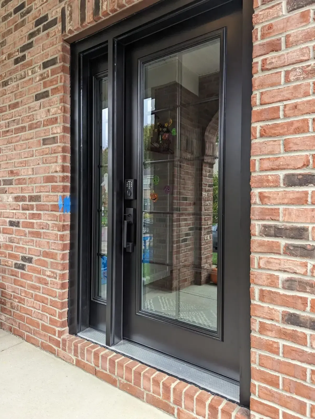 Black sliding glass door with digital keypad and aluminum frame installed in brick exterior wall